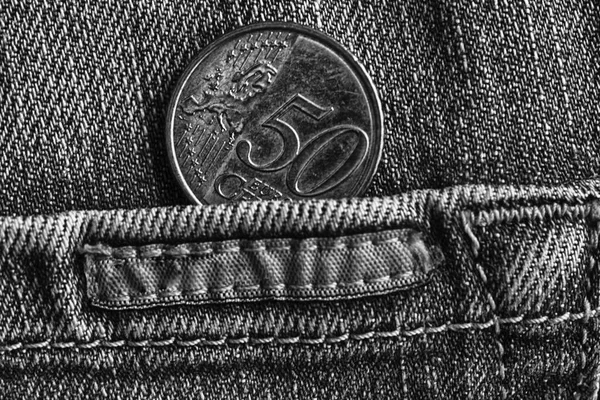 Euro coin with a denomination of 50 euro cents in the pocket of worn denim jeans with stripe, monochrome shot