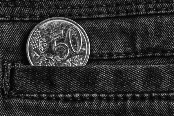 Euro coin with a denomination of 50 euro cents in the pocket of dark denim jeans, monochrome shot