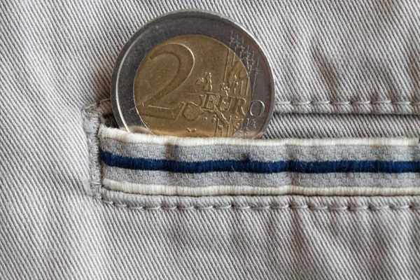 Euro coin with a denomination of 2 euro in the pocket of beige denim jeans with blue stripe — Stock Photo, Image