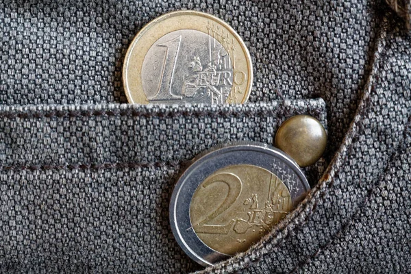 Euro coins with a denomination of 1 and 2 euro in the pocket of worn brown denim jeans