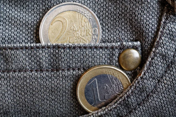 Euro coins with a denomination of one and two euro in the pocket of worn brown denim jeans