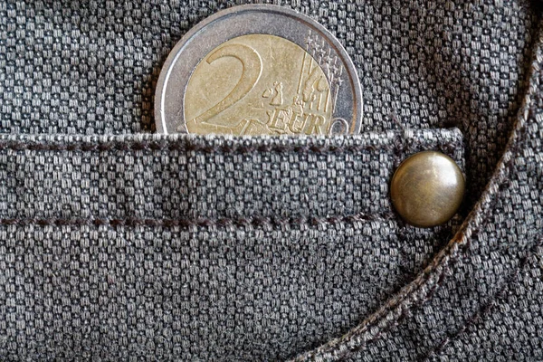 Euro coin with a denomination of two euro in the pocket of worn brown denim jeans