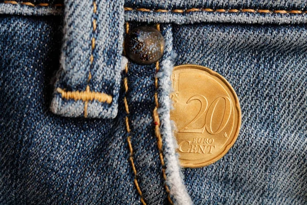 Euro coin with a denomination of twenty euro cents in the pocket of old worn denim jeans