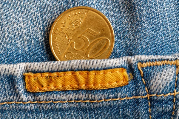 Euro coin with a denomination of 50 euro cents in the pocket of worn blue denim jeans with yellow stripe