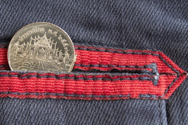 Thai coin with a denomination of five baht in the pocket of worn blue denim jeans with red stripe — Stock Photo, Image