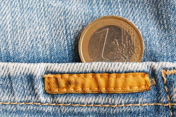 Euro coin with a denomination of one euro in the pocket of worn old blue denim jeans with orange seam