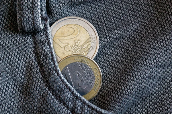 Two Euro coins with a denomination of 1 and two euro in the pocket of worn vintage brown denim jeans