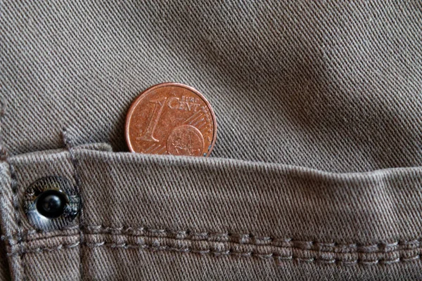 Euro coin with a denomination of 1 euro cent in the pocket of old worn gray denim jeans