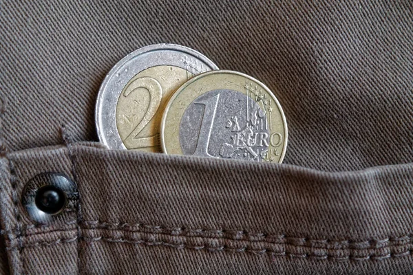 Two Euro coins with a denomination of 1 and 2 euro in the pocket of worn gray denim jeans