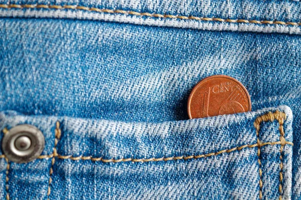 Euro coin with a denomination of one euro cent in the pocket of worn old blue denim jeans