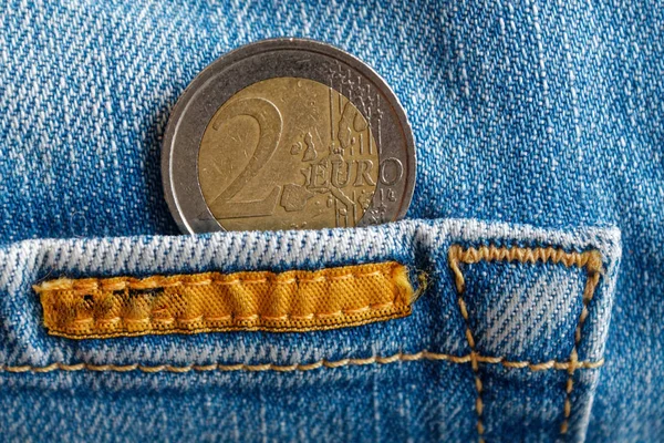 Euro coin with a denomination of two euro in the pocket of worn old blue denim jeans with orange seam