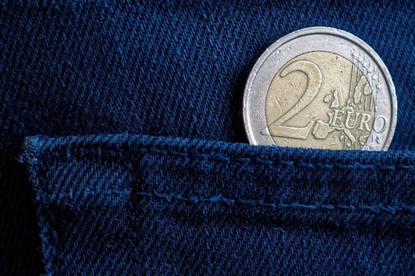 Euro coin with a denomination of 2 euro in the pocket of worn dark blue denim jeans