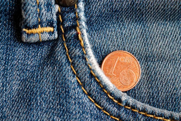 Euro coin with a denomination of 1 euro cent in the pocket of old worn blue denim jeans