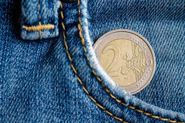 Euro coin with a denomination of two euro in the pocket of vintage worn blue denim jeans