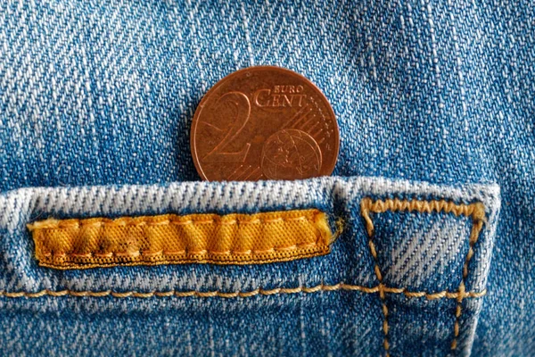 Euro coin with a denomination of two euro cent in the pocket of worn blue denim jeans whis orange seam