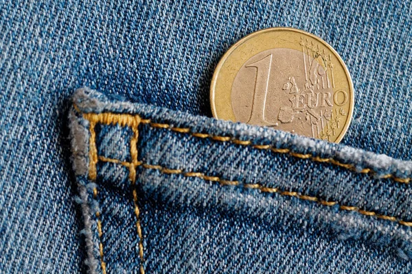 Euro coin with a denomination of one euro in the pocket of blue denim jeans