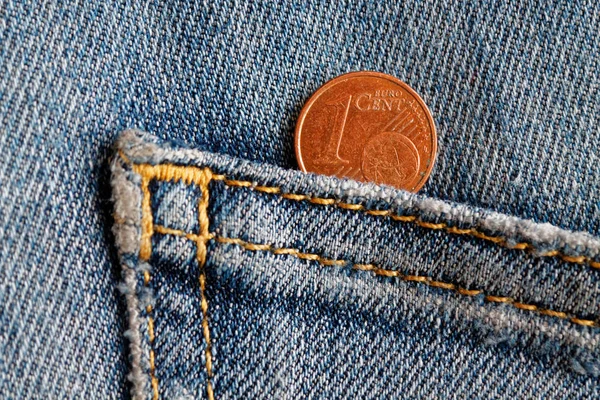 Euro coin with a denomination of one euro cent in the pocket of old blue denim jeans