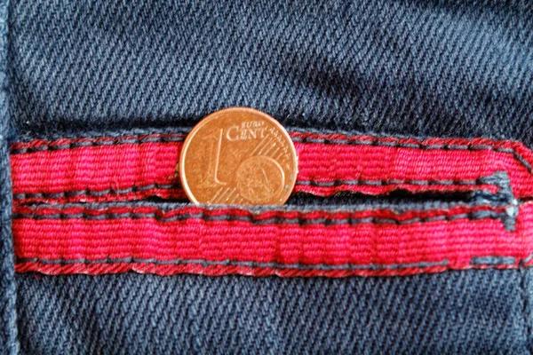 Euro coin with a denomination of one euro cent in the pocket of old worn blue denim jeans with red laces