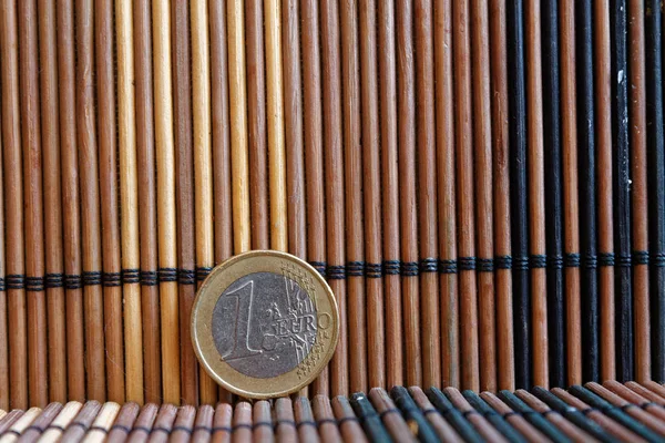 หนึ่งเหรียญยูโรนอนอยู่บนโต๊ะไม้ไผ่ การตั้งชื่อเป็น 1 ยูโร — ภาพถ่ายสต็อก