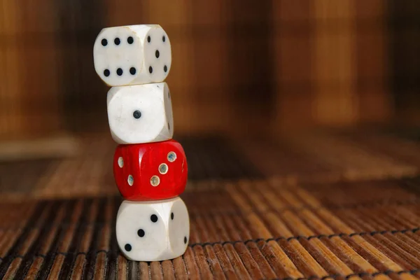 Stack of three white plastic dices and one red dice on brown wooden board background. Six sides cube with black dots. Number 1, 3, 6