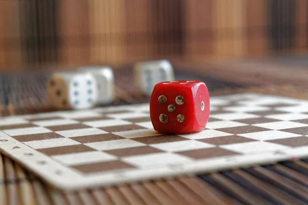 Verem a három fehér műanyag dobókocka és a barna fa sakktáblát háttér egy piros kocka. Kocka hat oldalán fekete pöttyökkel. 5-ös szám — Stock Fotó