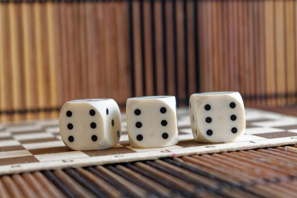 Verem a három fehér műanyag dobókocka barna fa sakktáblát háttér. Kocka hat oldalán fekete pöttyökkel. 6-os szám — Stock Fotó