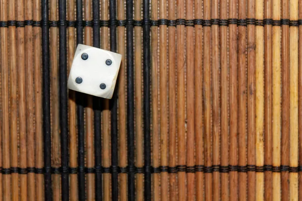 Um dado de plástico branco no fundo da placa de madeira marrom. Cubo de seis lados com pontos pretos. Número 4 — Fotografia de Stock