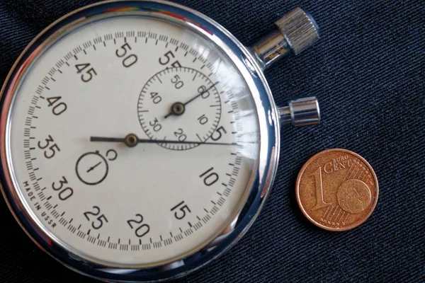 Euro coin with a denomination of one euro cent and stopwatch on black denim backdrop - business background — Stock Photo, Image