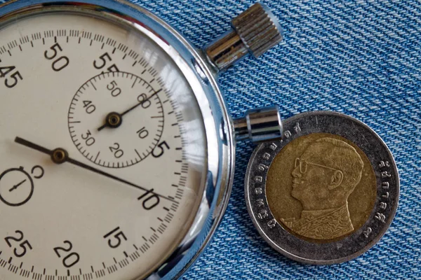 Thai coin with a denomination of ten baht (back side) and stopwatch on blue jeans backdrop - business background — Stock Photo, Image