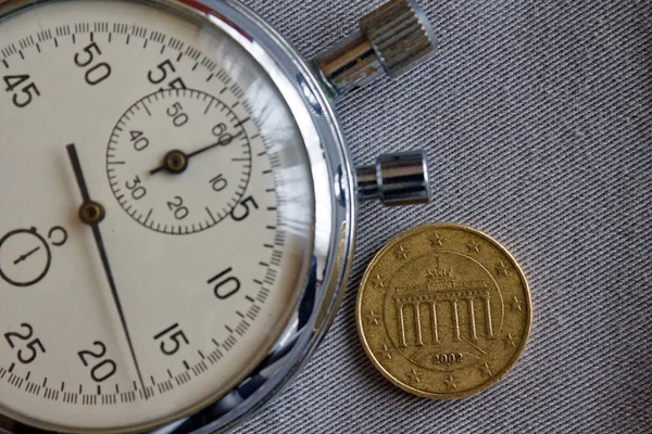 Euro coin with a denomination of ten euro cents (back side) and stopwatch on gray denim backdrop - business background — Stock Photo, Image