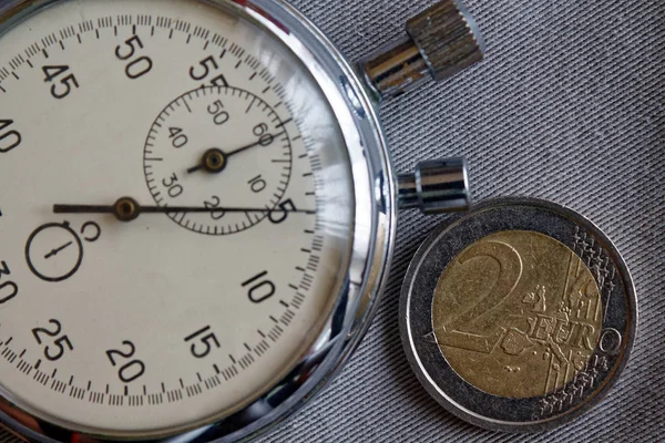 Pièce en euros avec une valeur unitaire de 2 euros et chronomètre sur fond de denim gris - arrière-plan d'affaires — Photo