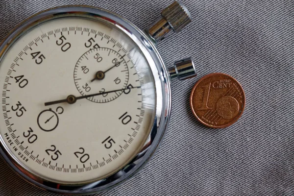 Euromunten met een nominale waarde van één eurocent en stopwatch op grijze denim achtergrond - zakelijke achtergrond — Stockfoto