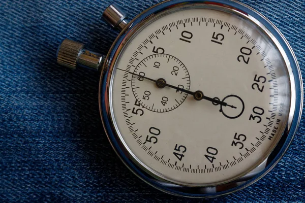Cronómetro en el fondo de mezclilla azul viejo desgastado, el valor mide el tiempo, el minuto de flecha del reloj viejo y el segundo registro de temporizador de precisión —  Fotos de Stock