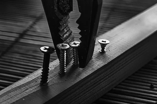Monochrome scattered screws screwed into the wooden plank and pliers — Stock Photo, Image