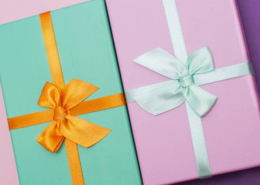 Flatlay with two colorful gift box with atlas ribbons on pink and purple background