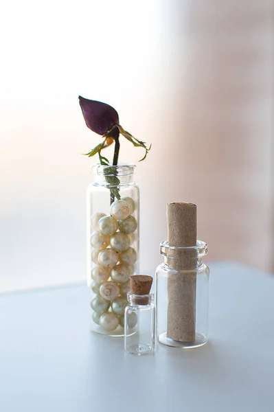 Primer plano de tres pequeños frascos de vidrio con perlas vintage, pergamino viejo y brote de rosa seca sobre fondo de ventana brillante — Foto de Stock