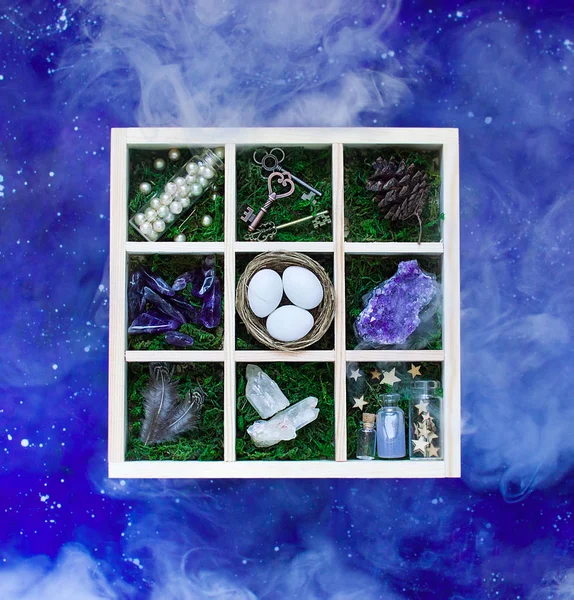 Flatlay of mysterious wooden witch box with moss and various things in it on a blue starry sky background with smoke — Stock Photo, Image