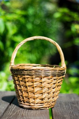 Ağaçların arkasındaki ahşap masada hasır sepetteki bezelye kabuklarının yakın plan çekimi.