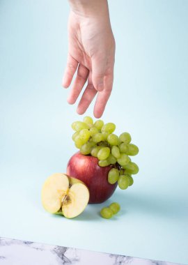 Üzüm dalı, mavi arka planda, büyük kırmızı elma dalında uzanıyor.