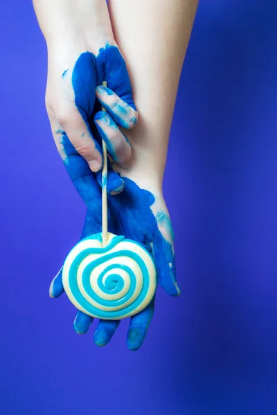 Руки Покрытые Синей Краской Держите Леденец Синем Фоне — стоковое фото