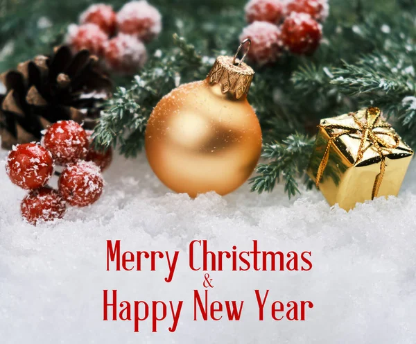 Рождественский фон с золотым рождественским мячом, подарочной коробкой, красными ягодами и елкой в снегу — стоковое фото