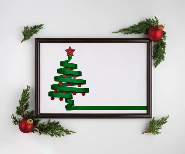 Stylized Christmas tree made from green ribbon with red shiny star and Christmas balls in photo frame on white background. Flat lay, top view, horizontal layout — Stock Photo, Image