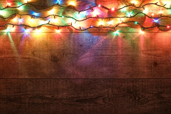 Christmas lights on wooden background. New Year festive decorations with colorful glowing Christmas lights. Colorful garland on wooden table. Flat lay, top view, horizontal layout — Stock Photo, Image