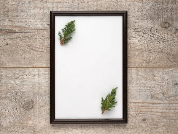 Fotolijstje met een vel wit papier met kopieerruimte en kerstboomtakken binnenin op houten ondergrond. Platte lay, uitzicht van bovenaf, verticale lay-out — Stockfoto