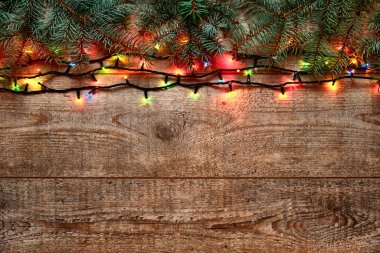 Noel ışıkları ve ağaç dalları ahşap arka planda. Renkli parlak Noel ışıklarıyla yeni yıl süslemeleri. Ahşap masada renkli bir çelenk. Düz yatıyordu, yukarıdan görüyordu