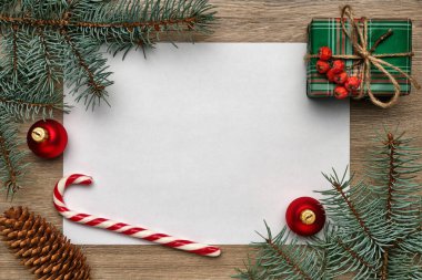 Yeni yıl ya da Noel kompozisyonu. Fotokopi alanı, hediye kutusu, şeker kamışı, Noel topu ve tahta zemin üzerinde köknar ağacı dalları olan beyaz bir sayfa. Düz yatıyordu, yukarıdan görüyordu