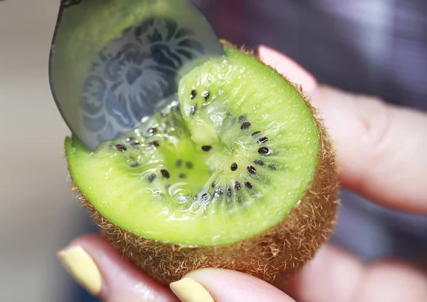 girl with beautiful nails is eating a ripe kiwi with a tea dessert spoon. Demonstration of kiwi fruit.