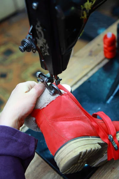 female hand of a shoemaker sew castle in boots