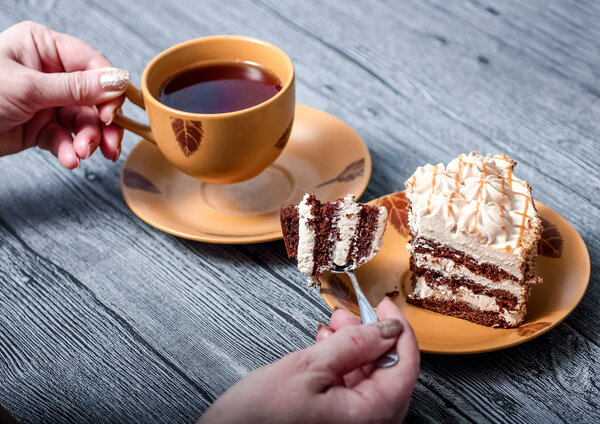 Man eats cake and drinks a Cup of tea sitting at a wooden table