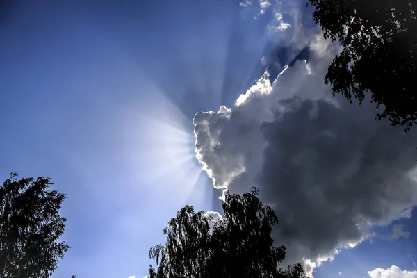 In the blue sky through the clouds rays of sunshine — Stock Photo, Image